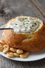 Vertical closeup of a bread bowl of New England Clam Chowder on a rustic wood table