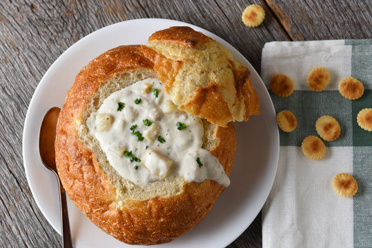 A bread bowl of New England Style Clam Chowder on a rustic wood table