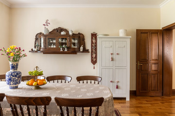 Wooden chairs at table with flowers in bright elegant dining room interior with door. Real photo
