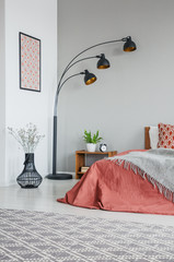 Vertical view of grey blanket on bed with cushions in bedroom interior with lamp and plants,real photo
