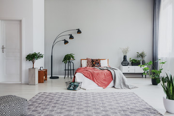 Full of trendy bedroom with comfortable king size bed, white wooden bed side table and plant, real...