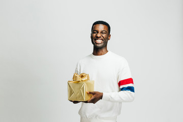 Portrait of a happy young man laughing and holding gold gift, isolated on white studio background