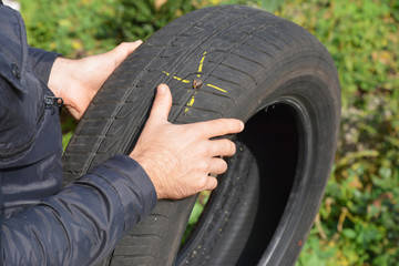 Fototapeta premium Car tire damage with nail and yellow mark. Flat car tire in the hands.
