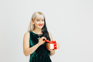 Portrait of a young blonde woman unwrapping golden gift with red bow