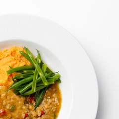 Top orner of a white plate with green beans, a lentil sause and mashed sweet potato.