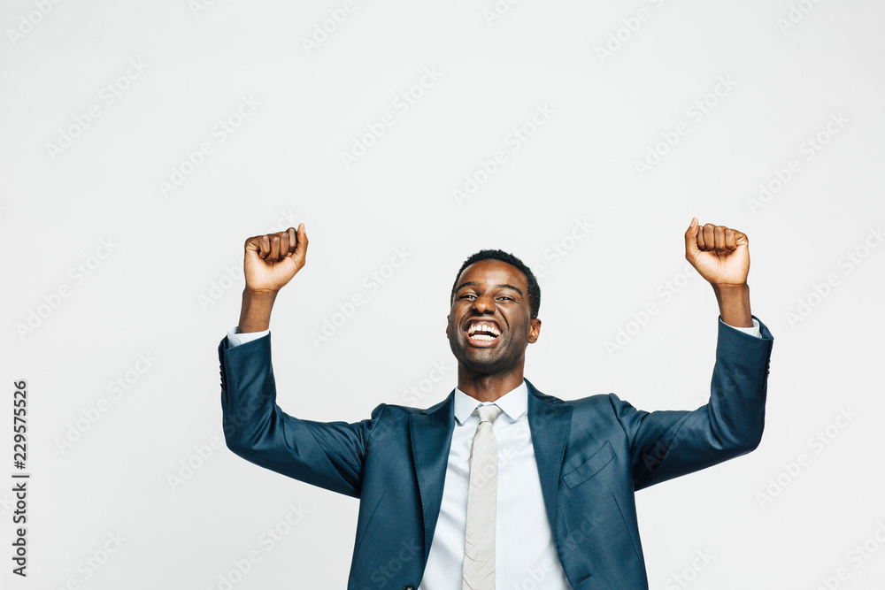 Wall mural celebrating success, portrait of a happy young man in business suit with both hands up, isolated on 