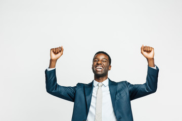 Celebrating success, Portrait of a happy young man in business suit with both hands up, isolated on white studio background