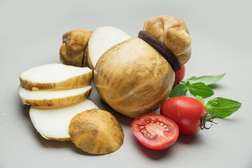 Traditional Italian smoked Scamorza cheese with herbs and tomatoes on gray background. © volff