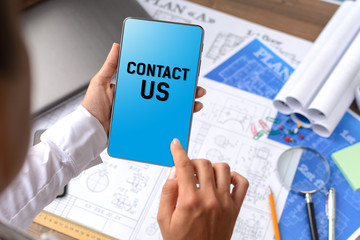 A girl (architect, student, businesswoman) at a table with business accessories, accessories for drawing (plans, rulers) and training with tablet with text Contact us