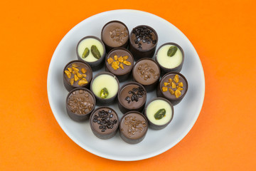 Chocolate candy on a white plate. Sweet beautiful candy lying on a plate on a bright color background.