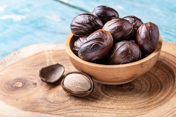 Whole nutmeg nuts in a bowl on blue rustic wooden table.