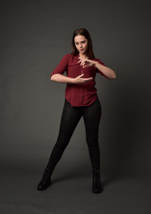 full length portrait of brunette girl wearing  red shirt and leather pants. standing pose, on grey studio background.