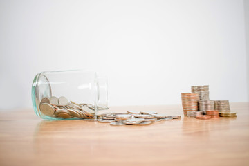 Side view of many coins in and outside the glass jar On a white desk, a white background.