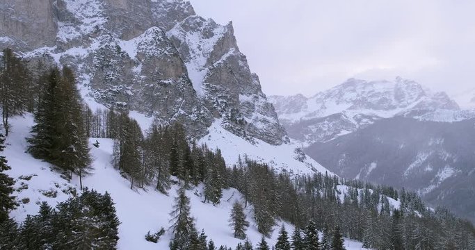 Forward aerial over woods forest with  snowy mountain.Cloudy bad overcast foggy weather.Winter Dolomites Italian Alps mountains outdoor nature establisher.4k drone flight establishing shot