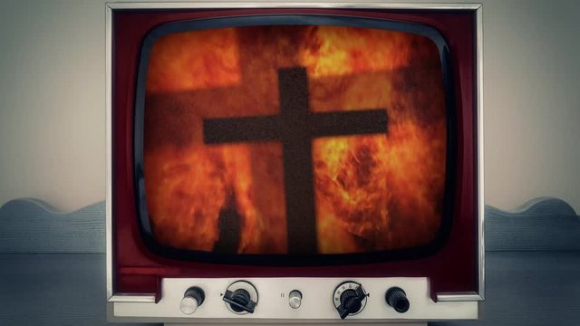 A retro vintage TV showing the double shadow of a Christian cross in front of a scary fire. Detail of the wild flames.
