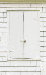 White weatherboard shingled exterior wall with closed shutters, pad locked & vintage hinges. Background, copy space