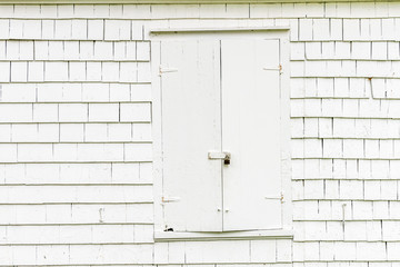 White weatherboard shingled exterior wall with closed shutters, pad locked & vintage hinges. Background, copy space