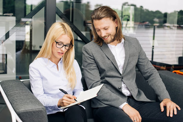 Businesswoman writes in agenda and businessman sitting by her