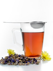 Vaso de cristal con te negro, flores y colador para infusiones