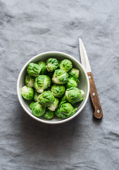Fresh brussels sprouts in white bowl on grey background, top view