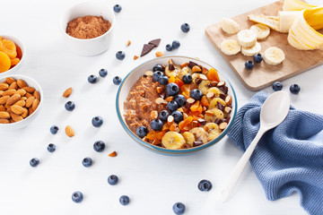 chocolate oatmeal porridge with blueberry, nuts, banana, dried apricot for healthy breakfast. Top view