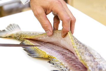 A chef filleting a zander with a knife on white chopping board.