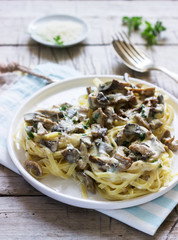 Tagliatelle with cream and forest mushrooms sauce in a white plate on a wooden background. Rustic style.