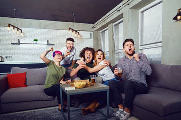 A group of friends are having fun watching TV in the room. Young people's fans spend their free time together.