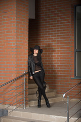 Young black dressed woman posing by a brick wall.