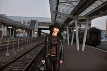 Obraz premium Young sexy woman dressed in black posing on a train station pier.