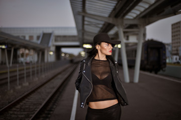 Young sexy woman dressed in black posing on a train station pier.