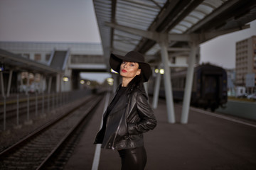 Young sexy woman dressed in black posing on a train station pier.