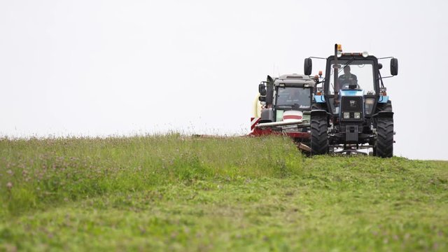 Line of agriculture tractorsriding on grass field at farm under gray sky on summer cloudy day
