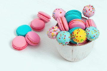 Fototapeta na wymiar Colorful sweet macaroons and cake pops in bowl on wooden white background with copy space. Food for party or dessert.
