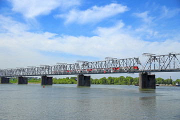 Fototapeta premium The train rides on the railway bridge against the sky with clouds in Novosibirsk