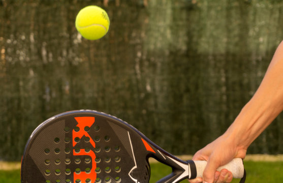 brazo con pala de padel y pelota en el aire y fondo verde