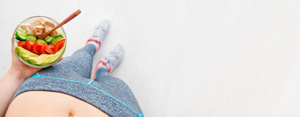 Young woman is resting and eating a healthy salad after a workout. Fitness and healthy lifestyle concept.