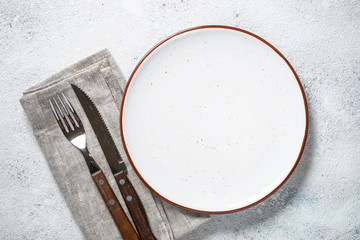 White plate and cutlery on stone table top view. 