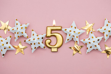 Number 5 gold candle and stars on a pastel pink background