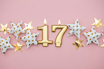 Number 17 gold candle and stars on a pastel pink background