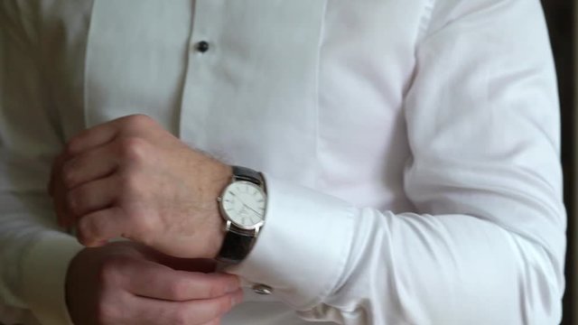 Businessman checking time on his wrist watch, man putting clock on hand, groom getting ready in the morning before wedding ceremony indoors