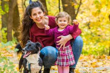 Naklejka na ściany i meble Happy Mother with her Baby Girl and her Dog in the Autumn Park .Mother and Daughter .Happy Family, Mother with Little Child and Dog in the Nature