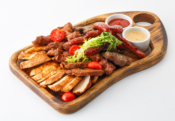 assorted sausages and meat with vegetables with mustard and ketchup on a wooden board isolated on white background