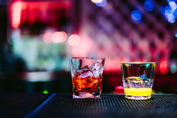 two glasses with cocktails on a rack of bar in night club