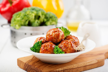 Meatballs with barbeque sauce and broccoli on wooden table.