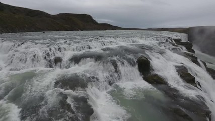 Aerial drone shot flying Gulfoss waterfall in Iceland. Cloudy day; low altitude flight, vertical view to horizon. - Powered by Adobe