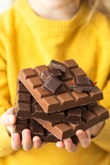Child in a yellow sweater holding chocolates. Unhealthy food concept