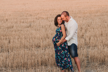 portrait outdoors of a young pregnant couple in a yellow field. Outdoors family lifestyle.