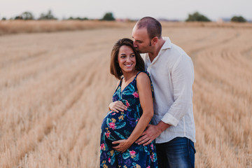 portrait outdoors of a young pregnant couple in a yellow field. Outdoors family lifestyle.