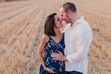 portrait outdoors of a young pregnant couple in a yellow field. Outdoors family lifestyle.